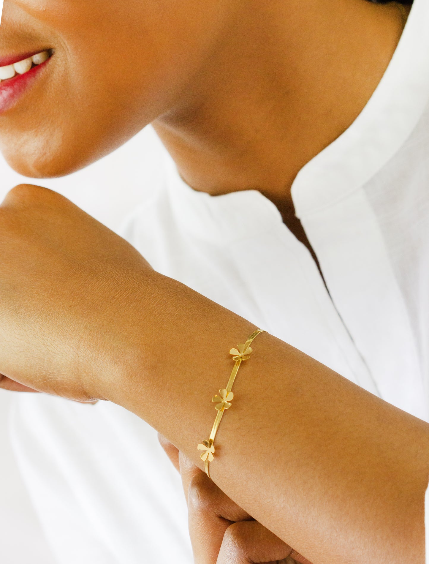 A close-up of a model's wrist showcasing a delicate gold bracelet with small flower charms from Dahlia Jewels. The model is wearing a white top, and the focus is on the elegant design of the jewelry. Dahlia Jewels offers free delivery in Nairobi.
