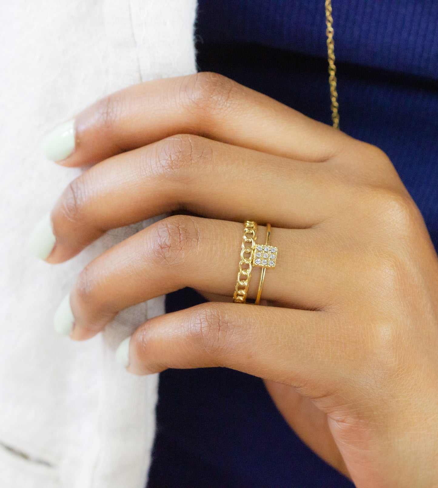 Close-up of a model's hand adorned with two elegant gold rings from Dahlia Jewels, featuring a delicate chain design and a square-set gemstone. Enjoy free delivery in Nairobi on all orders. Enhance your jewellery collection with these exquisite pieces.