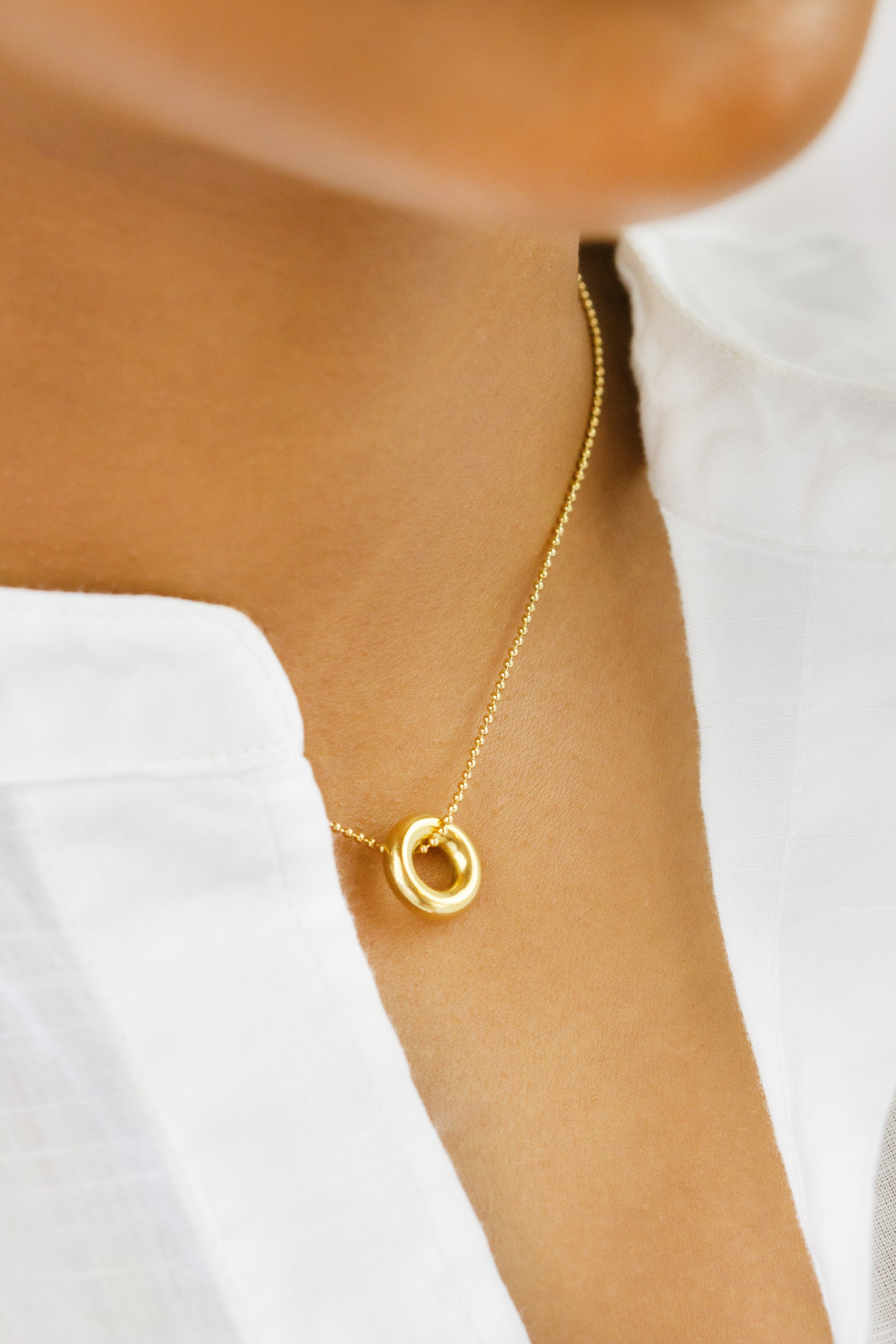 A close-up of a model wearing a minimalist gold necklace with interlocking circle pendants from Dahlia Jewels. The model is dressed in a white top, emphasizing the elegance and simplicity of the jewelry. Dahlia Jewels offers free delivery in Nairobi.