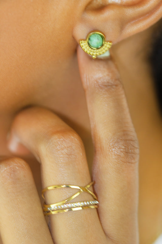 A close-up view of a model wearing a gold earring with a green stone and a stylish multi-band gold ring from Dahlia Jewels. Enjoy free delivery in Nairobi on all orders. Elevate your everyday look with these elegant jewellery pieces.