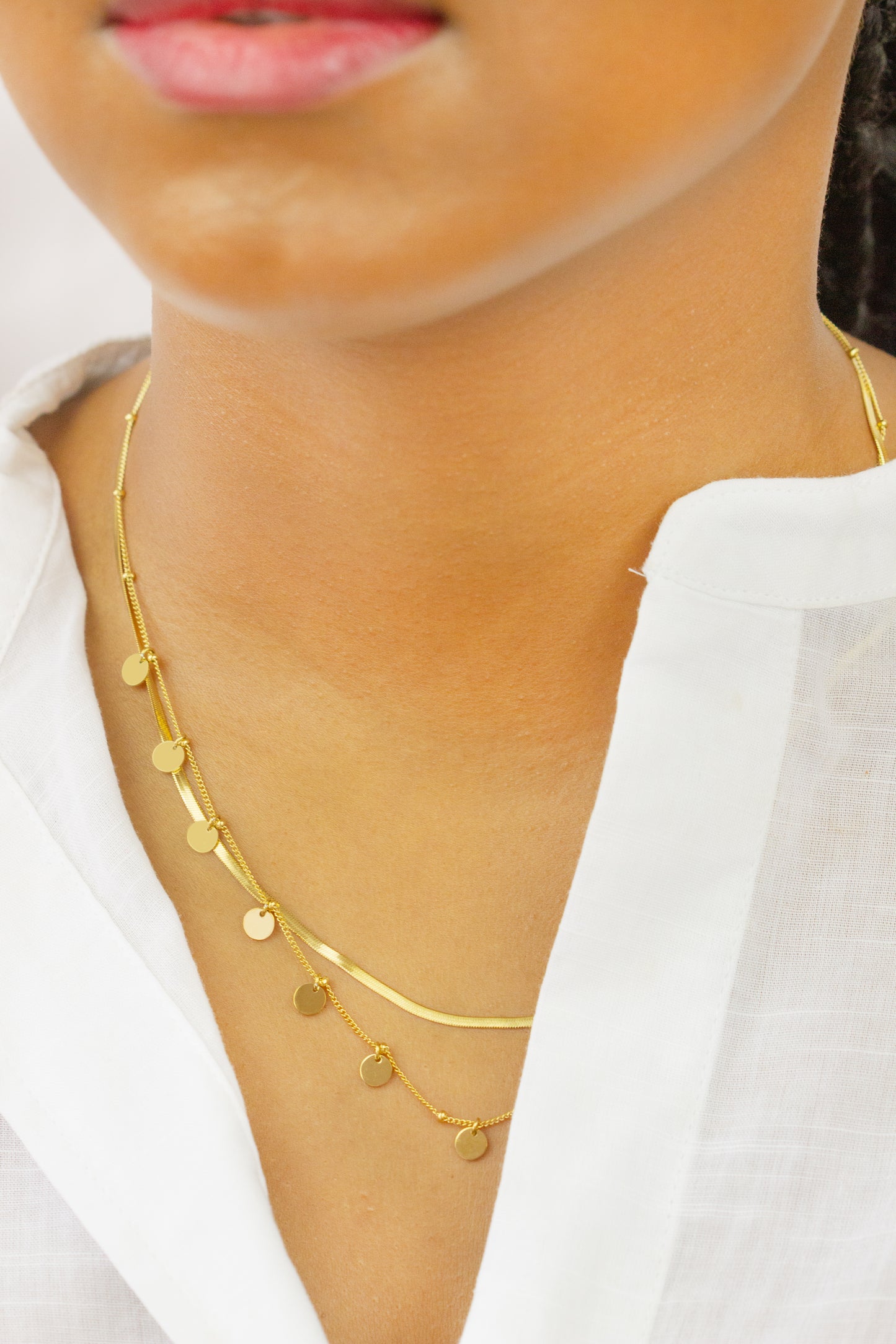 A model wearing a stylish gold double-layer necklace with small disc pendants from Dahlia Jewels. The necklace features two chains, one with a sleek design and the other adorned with dangling discs, perfectly complementing the model's outfit. Dahlia Jewels offers free delivery in Nairobi.