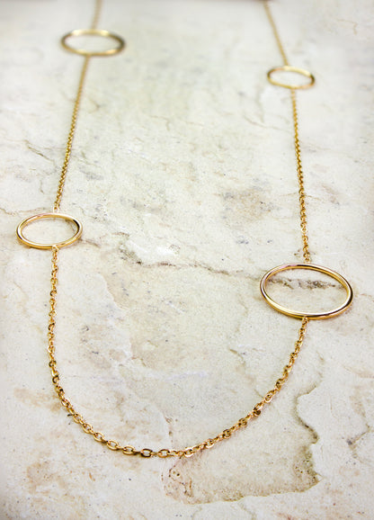Elegant long gold-plated necklace from Dahlia Jewels, featuring three large open circle charms spaced along its slender chain. This contemporary design marries simplicity with sophistication, ideal for enhancing any outfit with a touch of sleek, modern style. The circles’ clean lines and polished finish reflect a minimalist aesthetic, making it a versatile choice for both casual and formal occasions. Secures with a standard clasp. Available for free delivery in Nairobi. Keywords: jewellery, jewelry.