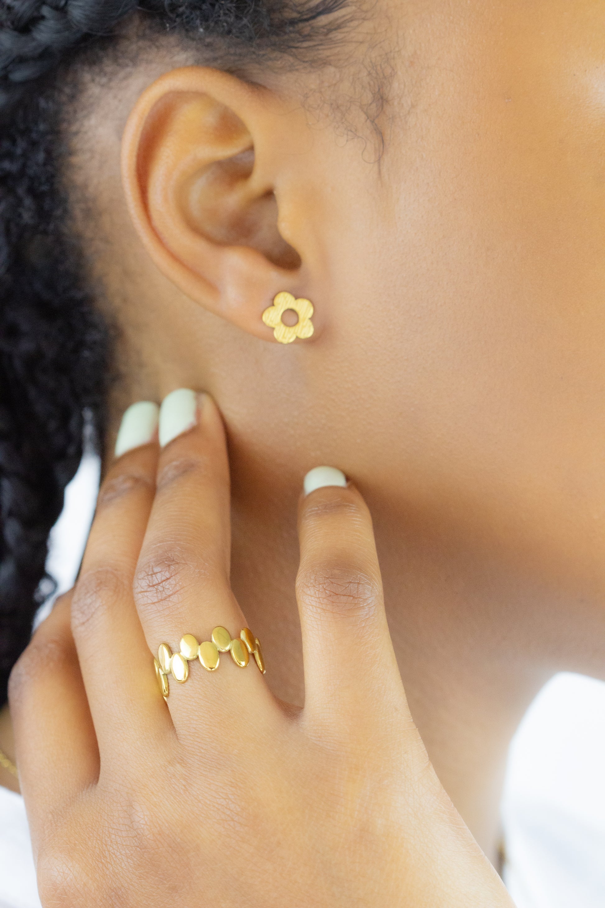 A close-up view of a model wearing a gold flower-shaped earring and a stylish gold ring from Dahlia Jewels. Enjoy free delivery in Nairobi on all orders. Elevate your everyday look with these elegant jewellery pieces.