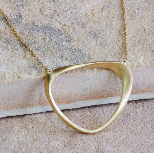 Elegant gold pendant necklace featuring a unique, open geometric design, displayed on a textured stone surface. The pendant has a smooth, matte finish, giving it a sophisticated and modern look. Available with free delivery in Nairobi. #gorgeouseveryday