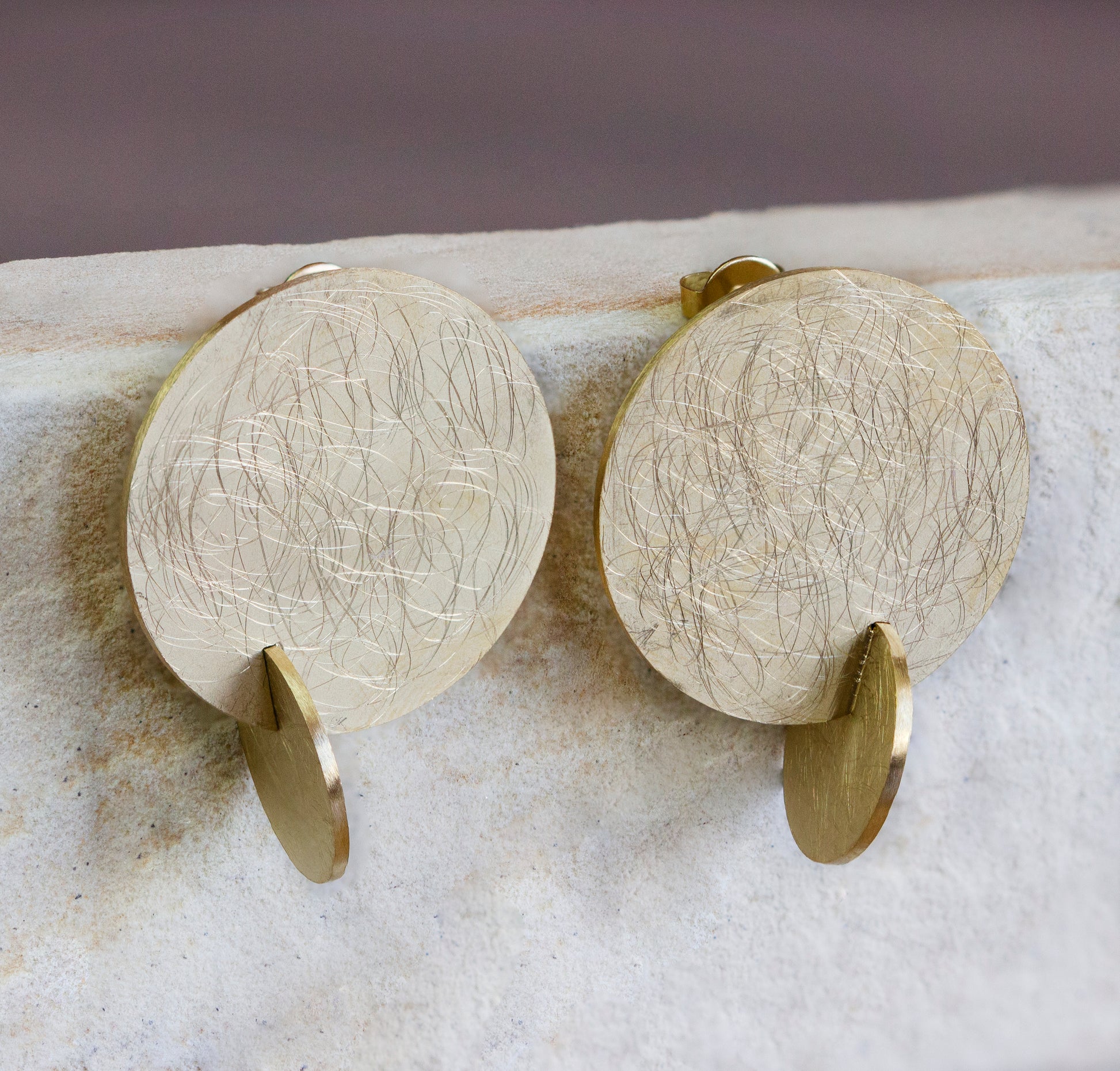 Contemporary gold stud earrings featuring large, textured discs with a scratched pattern and a small dangling accent. These bold earrings make a unique statement, perfect for elevating any look. Available with free delivery in Nairobi. #gorgeouseveryday