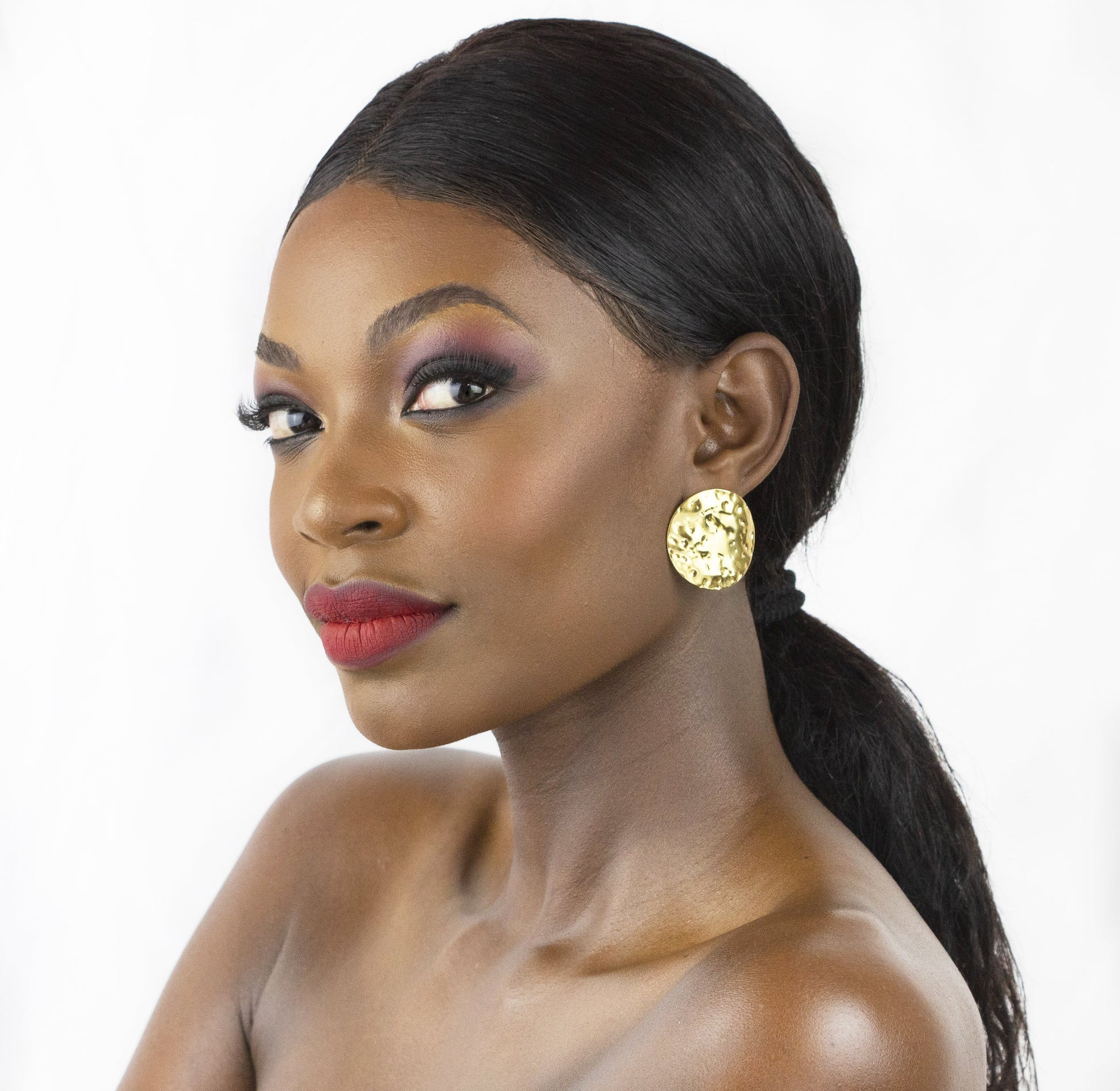 Model showcases Dahlia Jewels’ golden round earrings with an artistic hammered texture, reflecting intricate jewelry design. Free delivery in Nairobi.