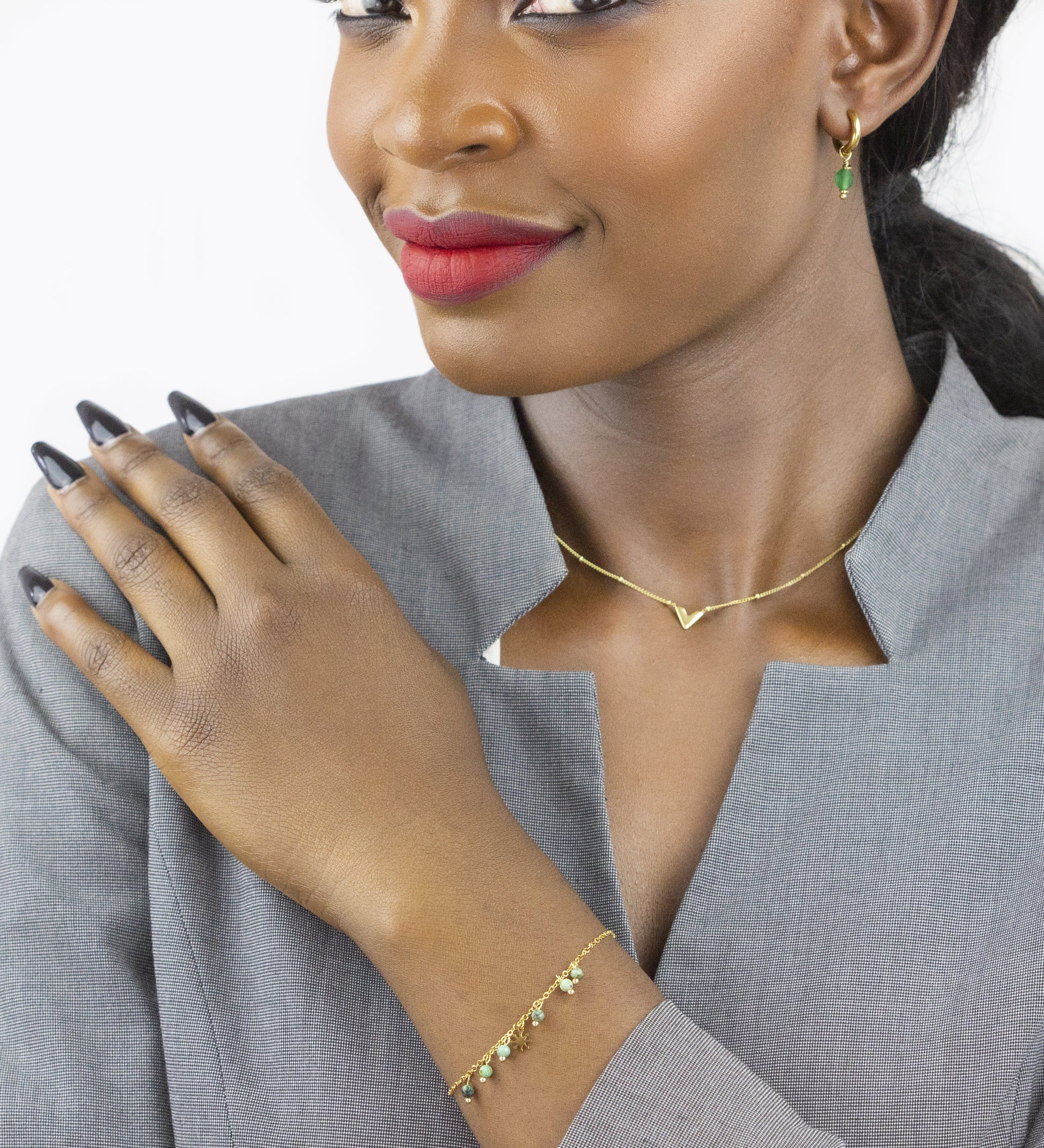 The model presents a gold-tone bracelet adorned with small gems from Dahlia Jewels on her arm, accompanied by a delicate gold necklace with a 'V' pendant and matching earrings, creating a coordinated look. Dahlia Jewels offers free delivery in Nairobi.
