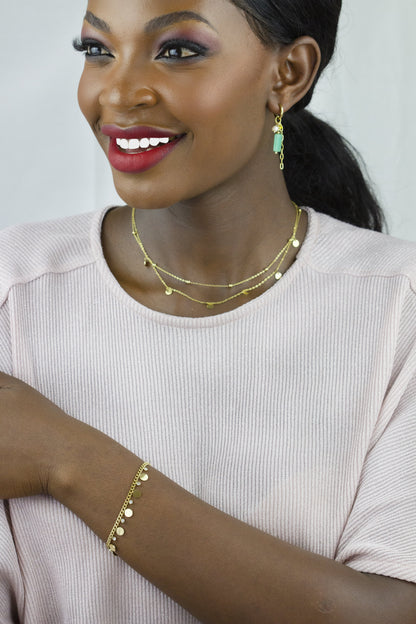 The model showcases a gold-tone bracelet from Dahlia Jewels on her arm, complemented by a layered gold necklace with small discs, adding a sophisticated touch to her look. The jewelry pairs perfectly with her attire. Dahlia Jewels offers free delivery in Nairobi.