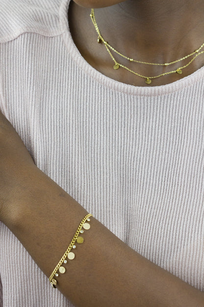 A model showcases a gold-tone bracelet and necklace from Dahlia Jewels. The bracelet is adorned with small discs and gems, while the necklace features a double-chain design with discs, adding an elegant touch. Free delivery in Nairobi.